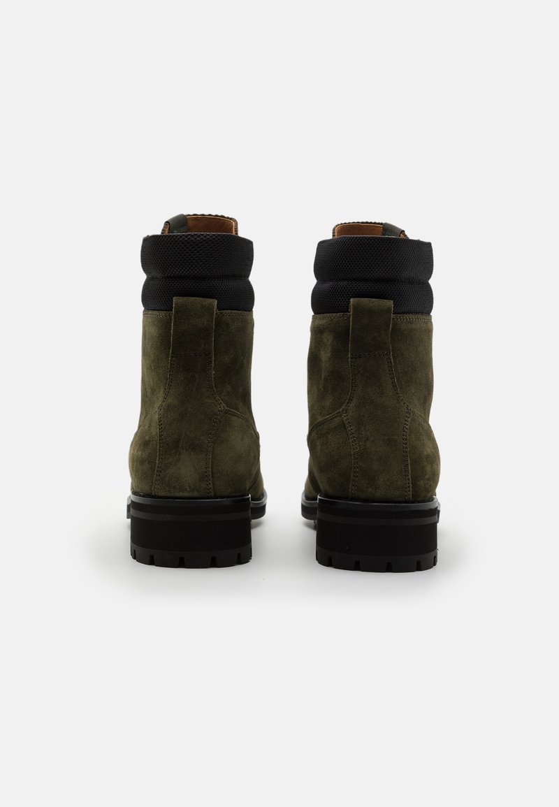 Ein Paar dunkelgrüne Wildleder-Ankle Boots mit schwarzen gepolsterten Kragen und dicken schwarzen Gummisohlen, von hinten auf einem weißen Hintergrund gezeigt.