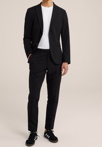 Svart blazer med slagkrage, matchad med svarta byxor och en vit T-shirt. Stylad med svarta sneakers med vita ränder.