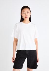 T-shirt blanche courte à manches courtes, col rond et texture de tissu lisse. Associée à un short en denim noir.