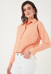 Oranje en wit gestreepte blouse met kraag en lange mouwen, met een ontspannen pasvorm en een borstzak, gecombineerd met witte broek.