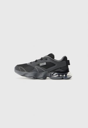 Chaussure de sport noire en matériaux en maille et synthétiques. Elle possède une semelle épaisse, des accents transparents et une marque bien visible sur le côté.