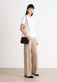Camicetta bianca a maniche corte, pantaloni beige a gamba larga e una borsa a tracolla nera. Tessuto liscio con linee pulite e design minimalista.