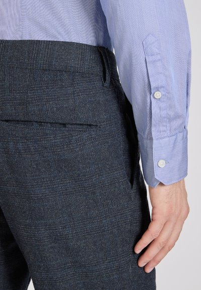 Niebiesko-biała w paski koszula z długim rękawem zestawiona z ciemnymi, strukturalnymi spodniami, które mają tylną kieszeń i subtelny wzór w kratkę.