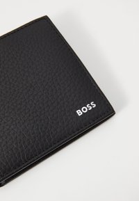 Black leather wallet featuring a textured surface, folded design, and white logo detailing. Compact shape with visible stitching.