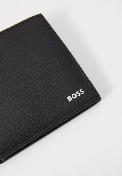 Portefeuille en cuir noir avec une surface texturée, design plié et détails du logo en blanc. Forme compacte avec des coutures visibles.