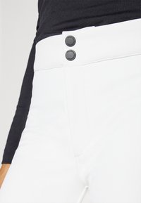 Witte fitted broek met een gladde afwerking, voorzien van twee zwarte knopen bij de taille en subtiele stiksels langs de naden.