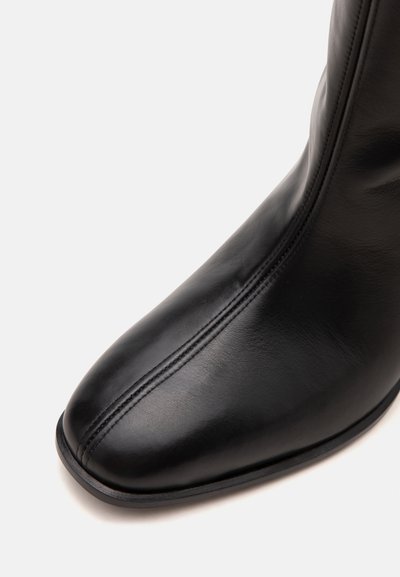 Gros plan d'une botte en cuir noire avec un bout carré et une couture verticale centrale sur la partie avant.