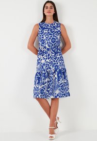 Blue and white patterned sleeveless dress with a fitted bodice and tiered skirt. Smooth fabric with a round neckline and casual silhouette.