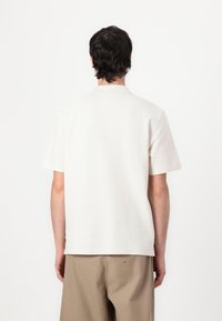 Short-sleeve, collared beige polo shirt in soft cotton fabric. Features a clean design with subtle texture, visible stitching, and no patterns.