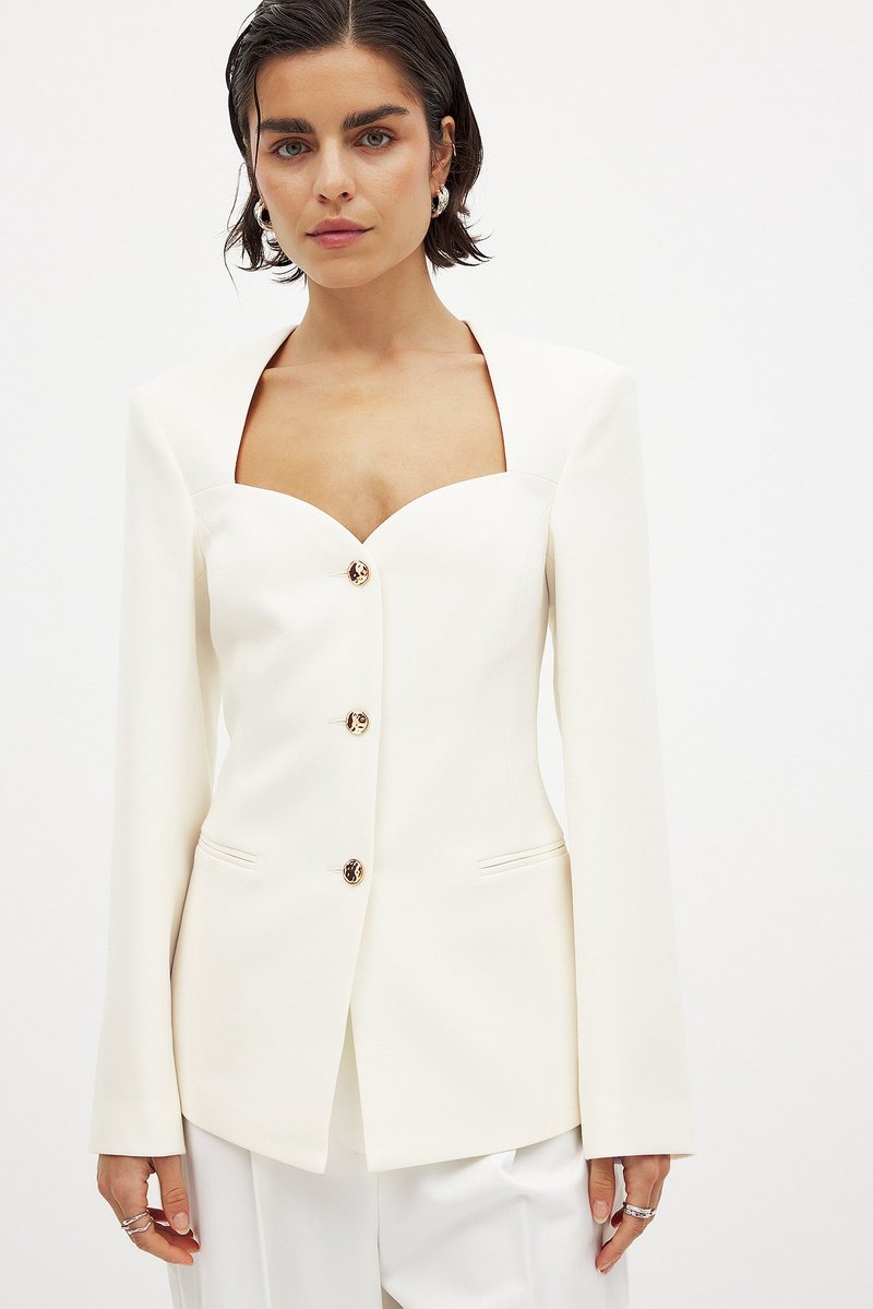 Balta struktūrēta žakete ar kvadrātu izgriezumu, ar vienu pogu un garām piedurknēm. Satur smalkas kabatu detaļas un gludu tekstūru.