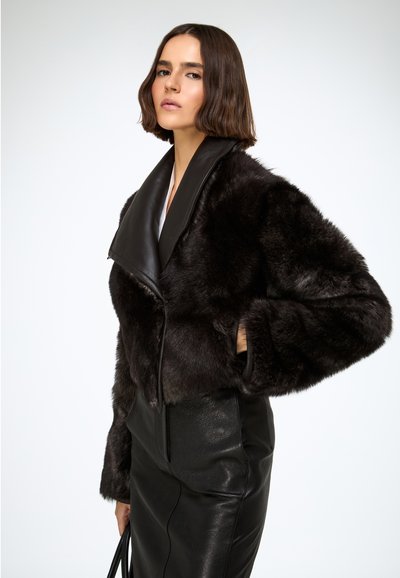 Skraćena jakna od crnog krzna širokog kožnog ovratnika, s dugim rukavima i bočnim džepovima, u kombinaciji s crnom kožnom suknjom.