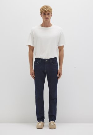 Weißes T-Shirt mit kurzen Ärmeln, kombiniert mit dunkelblauen Jeans. Die Jeans haben einen klassischen Schnitt und sind mit dezenten Nähten verziert.