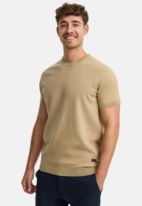 Suéter de punto de manga corta beige con cuello y puños acanalados. Textura suave, diseño ligeramente ajustado. Pequeña etiqueta de logo en la parte inferior izquierda.