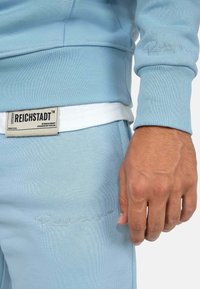 Felpa azzurra chiara e jogger coordinati realizzati in un morbido tessuto. Presentano polsini a coste, ricami e un'etichetta con il nome del marchio.