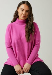 Maglione a collo alto rosa con un motivo di stelle in rilievo sul petto. Le maniche sono a coste e la vestibilità è rilassata, abbinato a pantaloni neri.