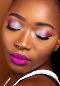 Lebendige lila Lippenstift, schimmernder Lidschatten in Blau- und Rosatönen, kräftiger Eyeliner und ein Nasenring auf glatter Haut.