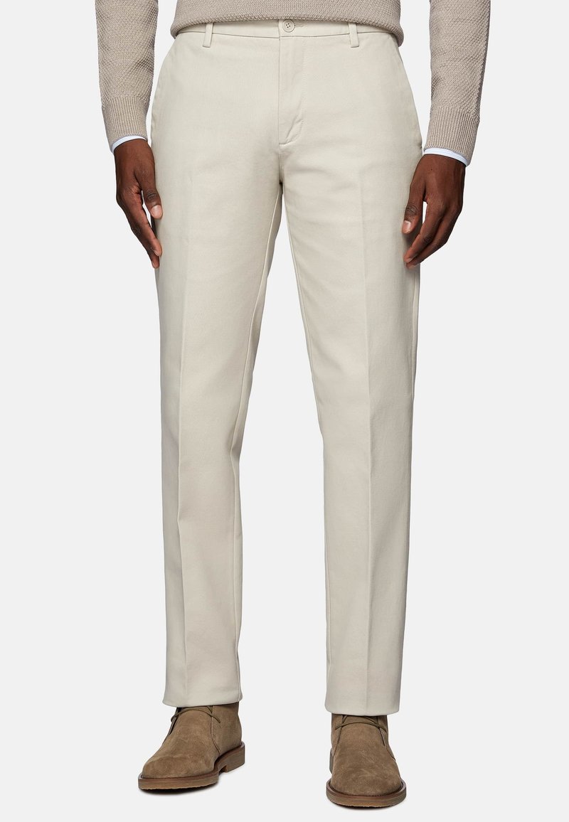 Beige chinos made of cotton blend, featuring a straight-leg design, two front pockets, and a smooth texture. Worn with brown suede boots.