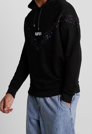 Sudadera con capucha negra con diseño moteado en púrpura y azul en el pecho. Presenta un logotipo "NASA" en la parte frontal y puños de canalé.