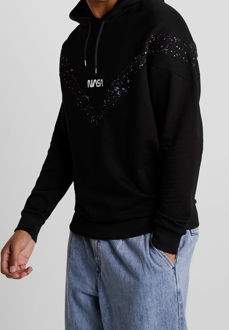 Sudadera con capucha negra con diseño moteado en púrpura y azul en el pecho. Presenta un logotipo "NASA" en la parte frontal y puños de canalé.