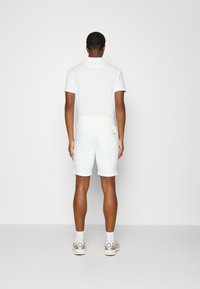 White polo shirt with short sleeves, paired with light-colored shorts. The shorts have a smooth texture and an elastic waistband.
