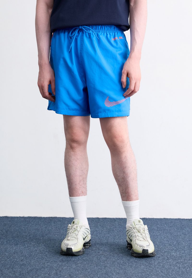 Modre atletske kratke hlače z elastičnim pasom in vrvico, na katerih je roza Nike logotip. Obute so z belimi nogavicami in svetlo obarvanimi teniskami.