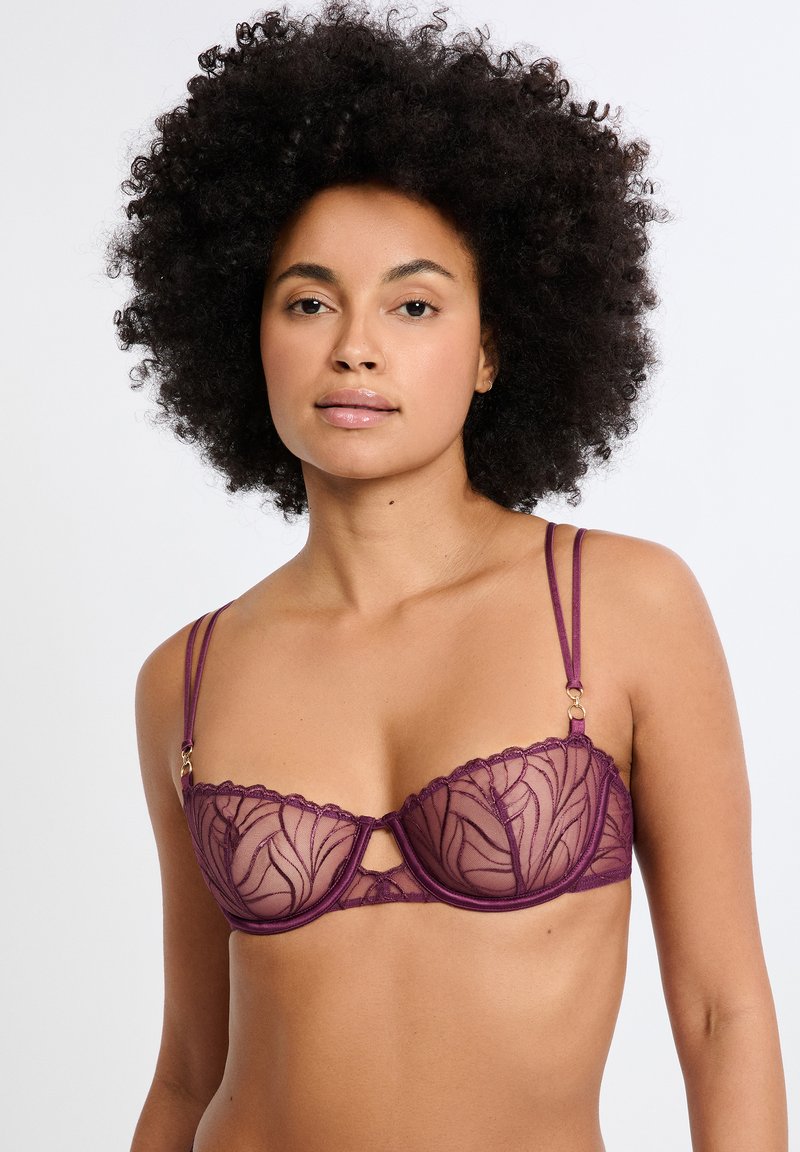 Soutien-gorge balconnet en dentelle violette avec motifs floraux, armatures, bretelles réglables et détail en ouverture au centre.