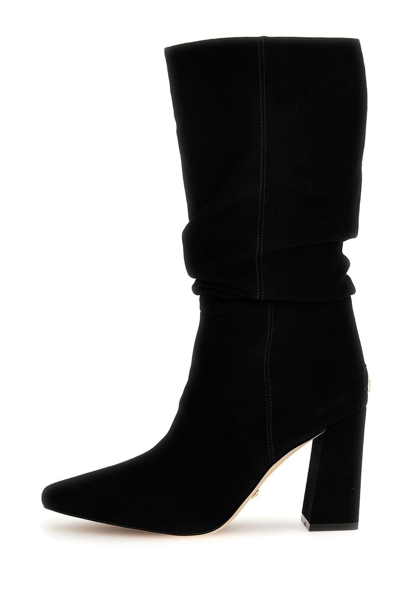 Zwarte, nonchalante enkellaars van zacht suède met een puntige neus en dikke blokhak. Heeft zichtbare sierstiksels en een subtiel gouden accent.