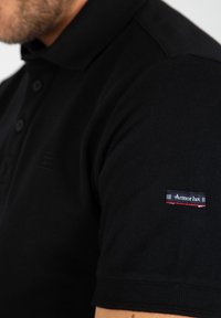 Zwarte polo in textuurstof, met een kraag en knoopsluiting, voorzien van een klein "Armor Lux" logo op de mouw.