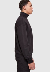 Svart høyhalset sweatshirt med lange ermer, ribbede mansjetter og en avslappet passform. Jevn tekstur uten synlige logoer eller mønstre.