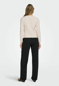 Beige langærmet sweater med rund hals, parret med løse sorte bukser og brune sko. Enkelt design med glat tekstur.