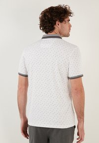 Polo majica s kratkimi rokavi v beli barvi z manjšimi sivimi vzorci. Ima kontrastni siv ovratnik in manšete. Narejena je iz zračnega materiala.