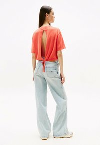 Koralfarvet t-shirt med åben ryg og bånddetalje, parret med lyseblå vide jeans. Blødt stof med en afslappet pasform.