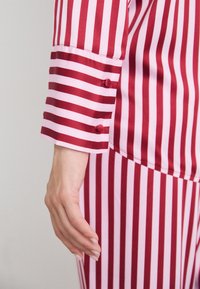 Red and pink striped pajamas feature a buttoned cuff and smooth fabric. The stripes alternate in width, creating a bold pattern.