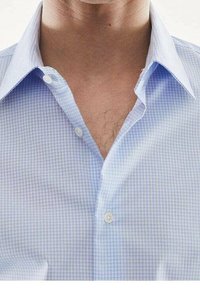 Chemise à carreaux bleu clair déboutonnée, dévoilant le cou et le haut de la poitrine avec des poils de poitrine visibles.