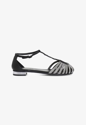 Black flat shoe with a T-strap design, embellished with silver rhinestones on the toe, and a low metallic heel for added detail.