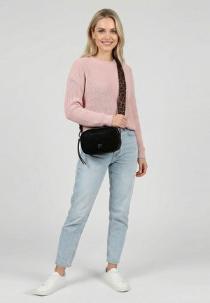 Moteris dėvi rožinį megztinį mezginį, šviesiai mėlynas džinsus, baltus sportinius batelius ir juodą per petį nešiojamą rankinę su leopardine spauda ant dirželio.