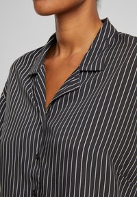 Camicia a righe bianche e nere con colletto, caratterizzata da una texture liscia e una vestibilità slim. Notevole motivo a righe verticali.