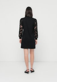 Black dress featuring long sheer sleeves adorned with floral appliqués. Simple silhouette with a round neckline and straight hem.