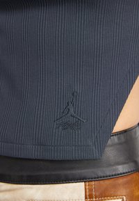 Top ribbed blu navy con un cinturino in pelle nera, caratterizzato da un logo Jumpman impresso vicino all'orlo e un dettaglio con taglio laterale.
