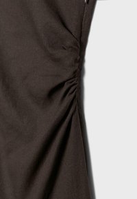 Tissu brun foncé avec un détail froncé rassemblé le long d'une couture, créant des plis texturés sur une surface lisse.
