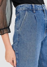 Jeans de mezclilla de tiro alto, color azul claro, con corte ajustado, que presentan costuras laterales acentuadas y un ligero desgaste cerca de los bolsillos.