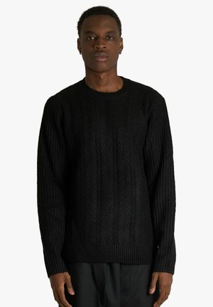 Maglione nero lavorato a maglia con texture a coste e motivo a spina di pesce, con scollo tondo e maniche lunghe.