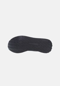 Sohle eines Schuhs, schwarzes Gummi-Material, strukturiert mit wellenförmigen Mustern für besseren Grip, mit flachem Profil und minimaler Markenkennzeichnung.