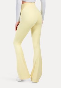 Żółte, rozszerzające się legginsy z wysokim stanem, wykonane z elastycznego materiału, charakteryzujące się gładką teksturą i brakiem widocznych wzorów czy akcentów.