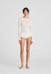 Top bianco a maniche lunghe, leggero, con un motivo testurizzato, abbinato a pantaloni corti beige. Il top presenta un collo rotondo e maniche aderenti.