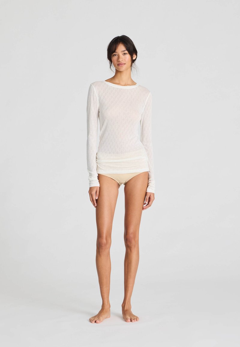 Top bianco a maniche lunghe, leggero, con un motivo testurizzato, abbinato a pantaloni corti beige. Il top presenta un collo rotondo e maniche aderenti.