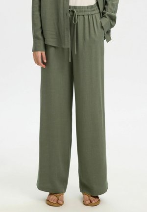 Olijfgroene wijde broek met elastische taille en trekkoord, gedragen met een bijpassend shirt en beige sandalen op een witte achtergrond.