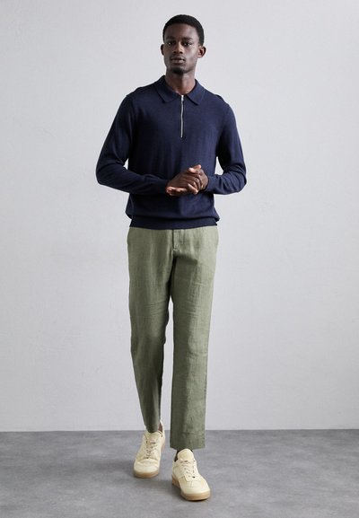 Marineblauer Poloshirt-Pullover mit Reißverschluss, hellgrüne Leinenhose und beigen Sneakers. Einfaches Design mit lockerer Passform und strukturiertem Stoff.