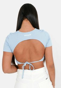 Lyseblå ribbet cropped top med korte ærmer og åben rygdesign, der har en knytning i taljen. Hvidt mærkeloft ved halsudskæringen.