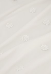 Witte stof met een zachte textuur, voorzien van kleine geborduurde bloemmotieven die gelijkmatig over het oppervlak zijn verspreid.